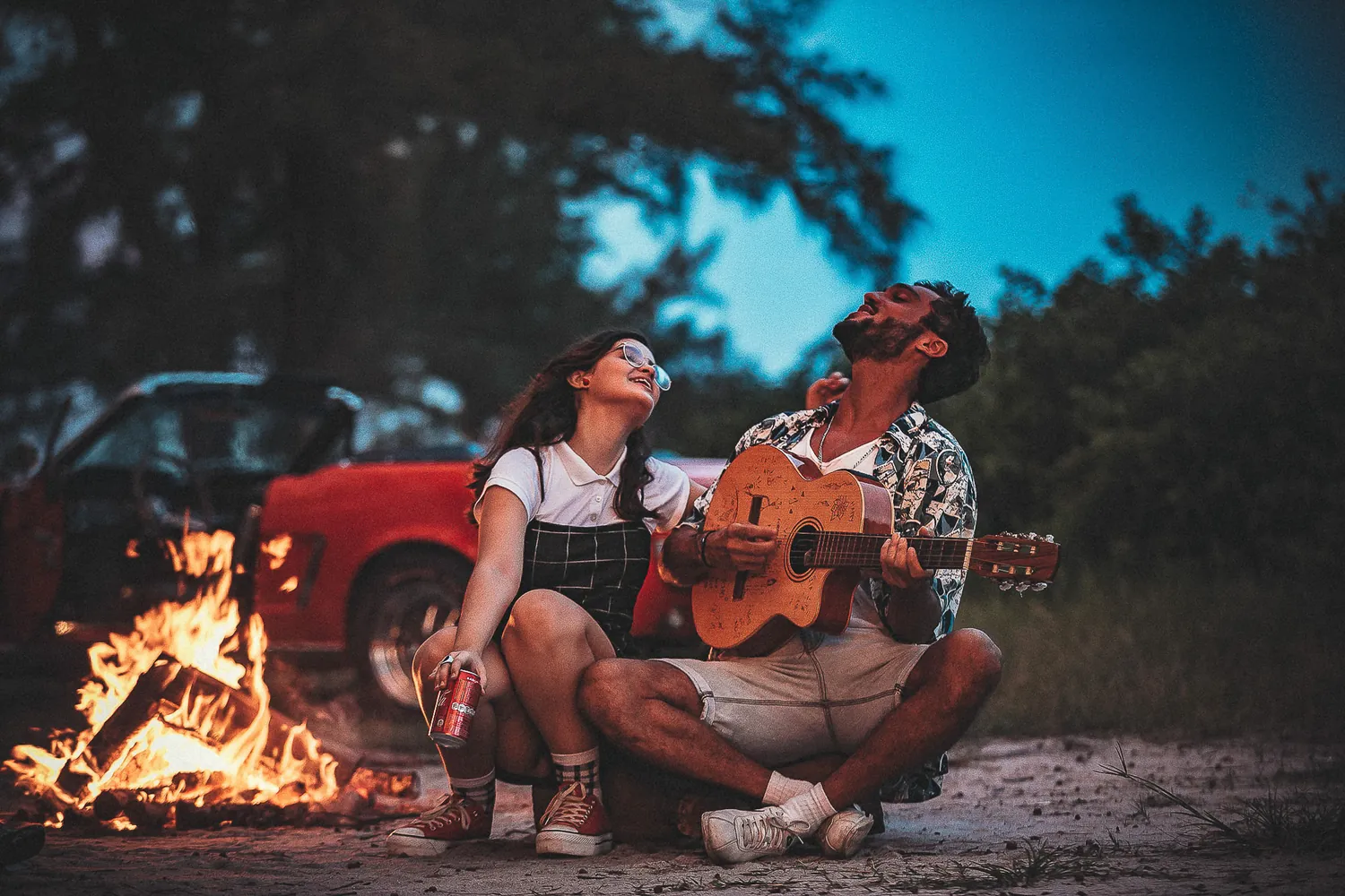 Couple playing guitar by a campfire